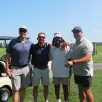 Four football alums standing in front of their golf cart.